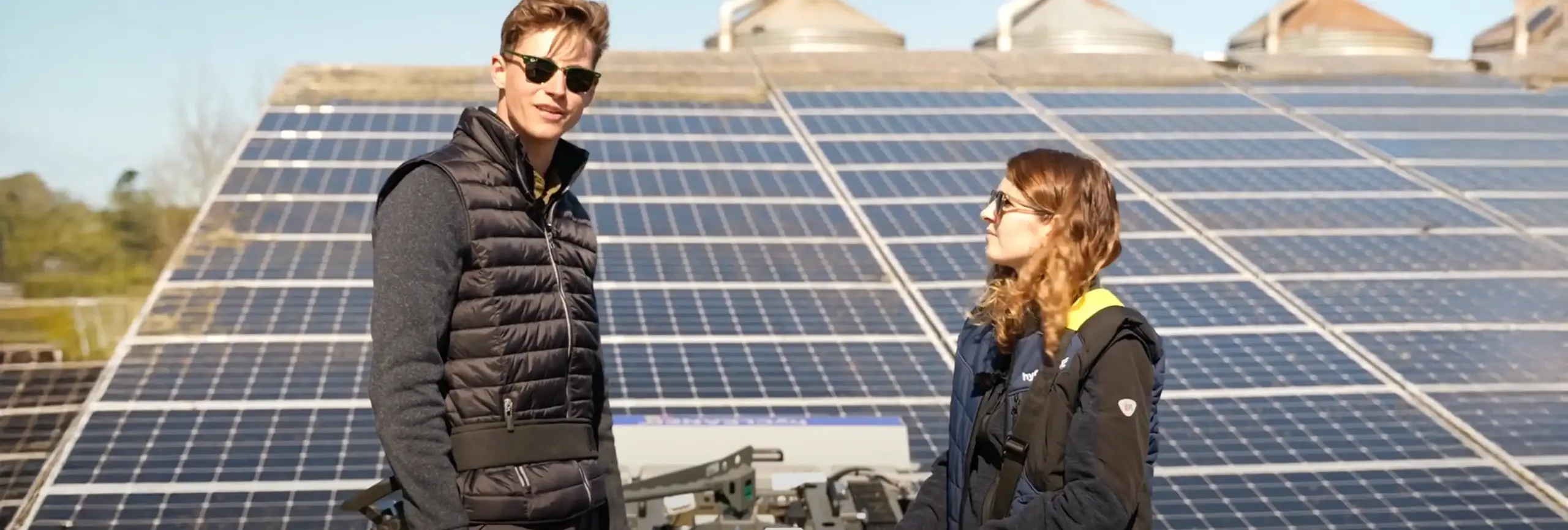 Two people stand in the sun in front of a PV system